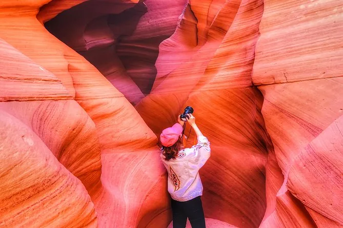A visitor photographing pink and orange sandstone in Antelope Canyon