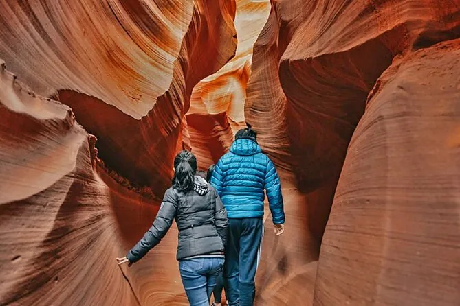 Two visitors in jackets walking through a narrow sandstone slot