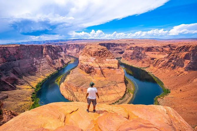 A traveler standing above Horseshoe Bend under a blue sky