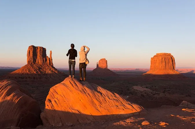 Dos viajeros sobre una roca viendo brillar los cerros de Monument Valley al atardecer