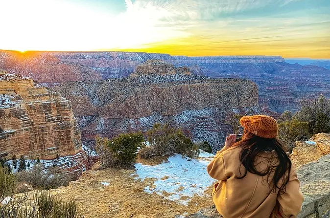 Eine Reisende im Wintermantel an einem verschneiten Aussichtspunkt am Grand Canyon